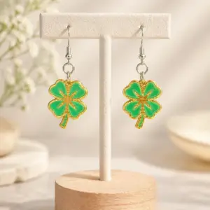 Green four-leaf clover drop earrings displayed on a neutral jewelry stand