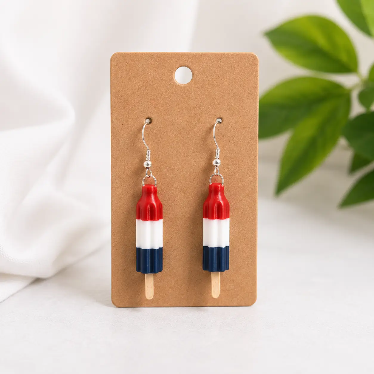 Handmade red, white, and blue Bomb Pop earrings displayed on a kraft jewelry card with a soft neutral background.