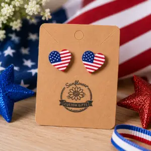 American flag heart stud earrings displayed on a Sunflower Custom Gifts jewelry card with patriotic decorations.